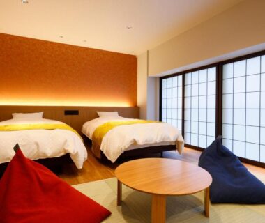 Tatami room with two beds, shoji screens, low round table and colorful bean bag chairs at Hanamandara Hyōgo