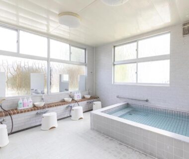 Bright indoor onsen with tiled soaking tub, wash stations, stools and large windows at Hanamizuki, Yamanashi