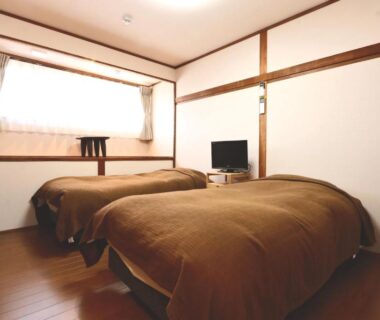 Two single beds with brown covers, wooden floor, low TV and curtained window in Hanamizuki ryokan room