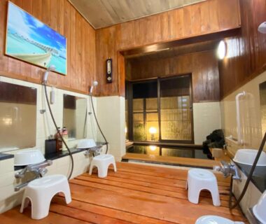 Indoor washing area with wooden floors, stools, handheld showers and shoji screen doorway at Hanamizuki Onsen Resort in Shizuoka
