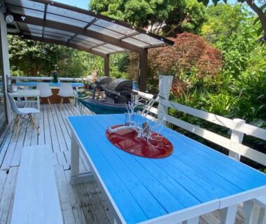 Outdoor wooden deck with blue table, red centerpiece fountain, white benches and lush garden in Shizuoka