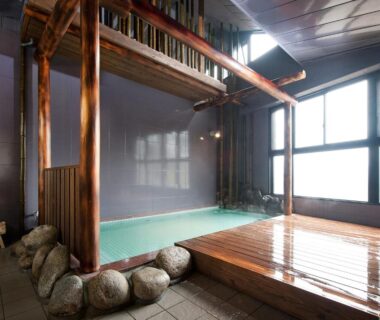 Indoor onsen with wooden deck, timber pillars, stone edging and large window at Hanano Koyado Jyu-bei, Mie