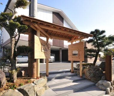 Wooden entrance gate with stone path, trimmed pines and parked cars at Hanano Koyado Jyu-bei in Mie prefecture