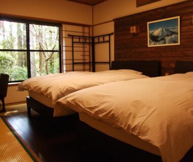 Interior with two raised beds on wooden platform, tatami flooring, shoji screen window overlooking greenery, framed wall artwork