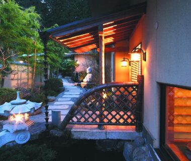 Evening lantern-lit stone path leading to wooden ryokan entrance with shoji window and small garden in Kanagawa