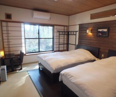 Tatami-floored guest room with twin beds, shoji window, wooden accent wall and desk at Hananoyado Fukuya, Kanagawa