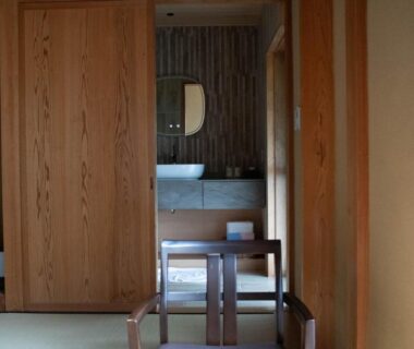Interior tatami room with wooden sliding doors, sink vanity visible through doorway, simple chair and low table