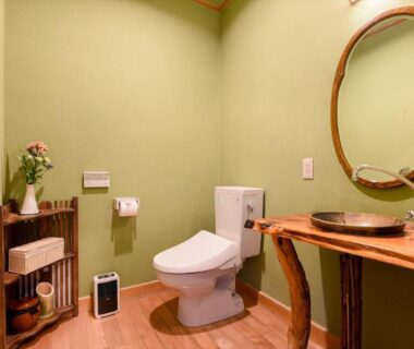 Compact restroom with modern toilet, wooden sink counter, round mirror and green walls at Hanare Yado Yosizumi Shizuoka