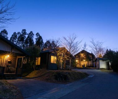 Lit wooden cottages along a quiet road at dusk, Hanare no Yado Hanagokoro, Kumamoto