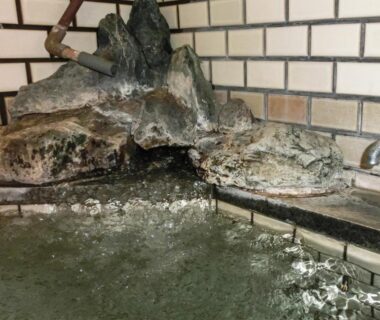 Indoor onsen bath with rock water spout and tiled walls at Hanasaku Onsen Yoshiyaso, Gunma