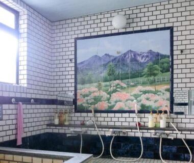 Indoor communal tiled onsen bath with mountain mural and shower stations at Hanasaku Onsen Yoshiyaso Gunma