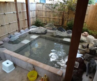 Small outdoor stone onsen bath with bamboo fence, washing stools and buckets at Hanasaku Onsen Yoshiyaso, Gunma