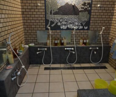 Communal washing stations with stools, handheld showers and mosaic wall art at Hanasaku Onsen Yoshiyaso, Gunma
