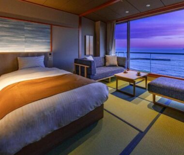 Twin beds on tatami with low table and large window revealing ocean sunset at Hanashibuki, Chiba, Kantō