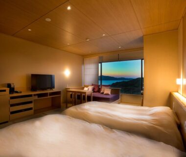 Twin beds and seating area with large window overlooking distant mountains at Hanashinsui in Mie, Kansai