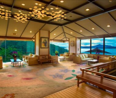Spacious lounge with low seating, large windows and wooden soaking tub overlooking bay and hills in Mie