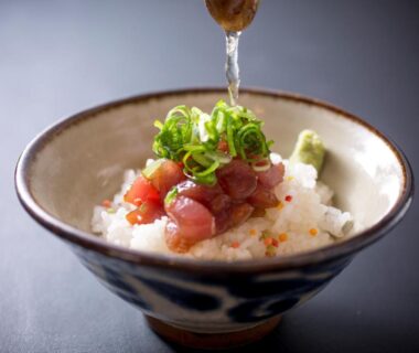 Rice bowl topped with diced raw fish, scallions, wasabi, and soy sauce being poured