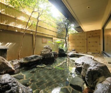 Rock-lined outdoor onsen with bamboo fence and sliding shoji doors at Hanasuishou, Yamanashi, Chūbu