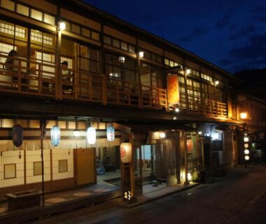 Lit traditional wooden ryokan facade with paper shoji windows and lanterns along a quiet Nara street at dusk