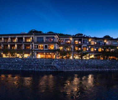 Night view of illuminated riverside ryokan building reflecting on river at Hanayashiki Ukifune-en in Kyoto