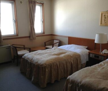 Two single beds with bedside lamp and chairs in Happokan guest room, Nagano, Chūbu, Japan