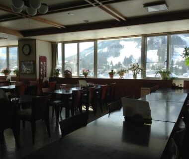 Spacious dining area at Happokan with wooden tables, large windows and snowy mountain views in Nagano