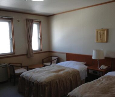 Two single beds with lamp and window seating in a simple Happokan guest room in Nagano