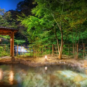 Steamy stone outdoor onsen with red umbrella, bamboo fence and trees at night, Harataki Fukushima Tohoku