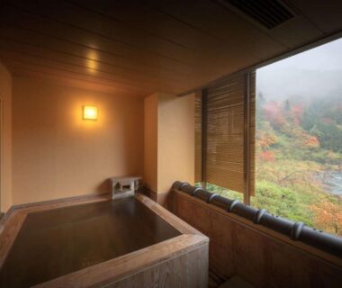 Indoor wooden onsen bath overlooking river and autumn foliage at Harumiya Ryokan Fukushima