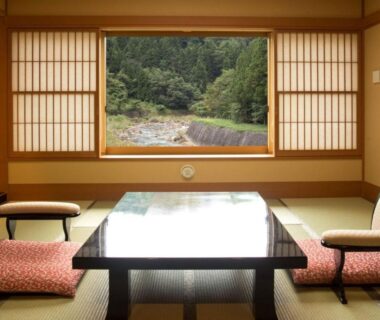 Tatami room with low table and shoji window overlooking a river at Harumiya Ryokan in Fukushima