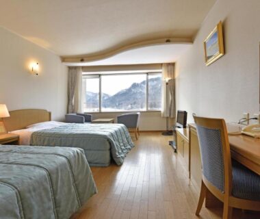 Twin beds in a bright room with wooden floor, desk and mountain view at Harunako Onsen Yusuge, Gunma