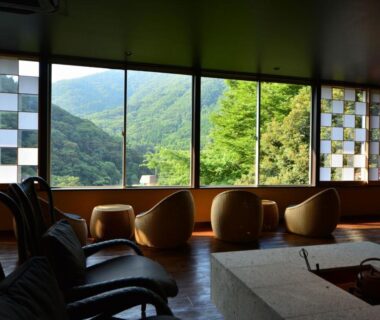 Low curved armchairs by panoramic windows overlooking green mountains at Hatago Kintoen, Kanagawa