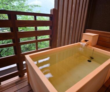 Wooden soaking tub on balcony overlooking green trees at Hatago Kintoen ryokan in Kanagawa