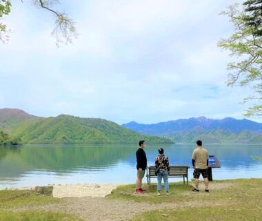 Three people by a calm lakeshore with benches at Hatago Nagomi in Tochigi