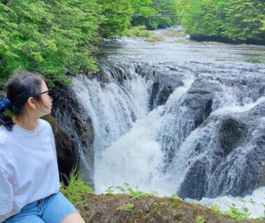 Person seated on riverside rock beside cascading waterfall near Hatago Nagomi Tochigi