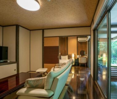 Interior lounge with sofas, polished wooden floor and sliding glass doors opening to garden at Hatago Sakura in Ōita