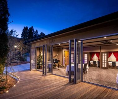 Wooden deck with folding glass doors opening to dining room at Hatago Sakura in Ōita under twilight sky
