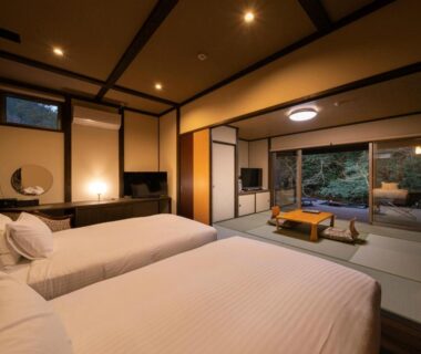 Tatami room with twin beds, low wooden table and garden-facing sliding doors at Hatago Sakura, Oita