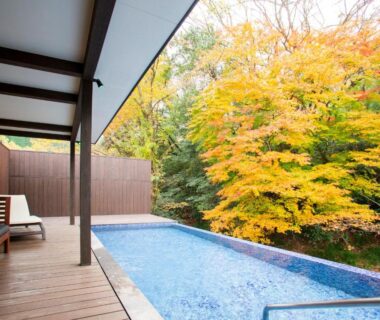 Outdoor pool and wooden deck with lounge chairs beside autumn maple trees at Hatago Sakura, Ōita, Kyūshū