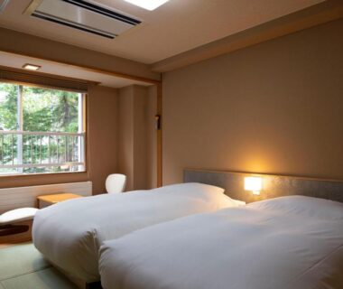 Tatami room with twin beds, low table and leafy window view at Hatagoya Jozankei Shoten Hokkaidō