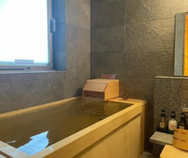 Indoor wooden soaking tub with stone tile walls, small window and toiletries at Hatagoya Jozankei Shoten, Hokkaidō Japan