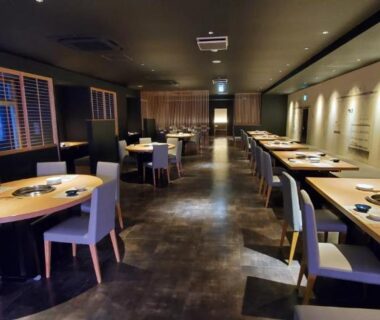 Spacious ryokan dining hall with round and rectangular tables, soft lighting and polished floor at Hatagoya Jozankei Shoten, Hokkaidō