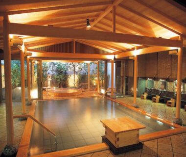 Spacious indoor onsen with timber beams, tiled floor and seating area at Hatori in Chūbu, Ishikawa