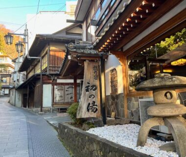 Exterior entrance with wooden sign and stone lantern along narrow street at Hatsunoyu, Nagano
