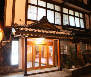 Warmly lit traditional ryokan entrance with wooden facade at Hatsunoyu in Nagano, Chūbu