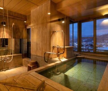 Indoor wooden onsen bath with large window overlooking city and mountains at Hayamakan Yamagata