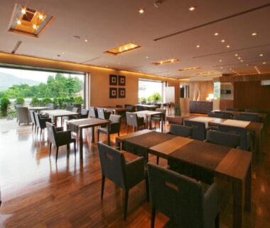 Dining area with wooden floors, tables and large windows overlooking greenery at Hayamakan, Yamagata