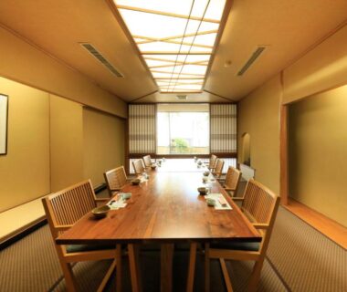 Long wooden dining table and chairs on tatami, shoji screens and alcove with hanging scroll at Hayamakan, Yamagata