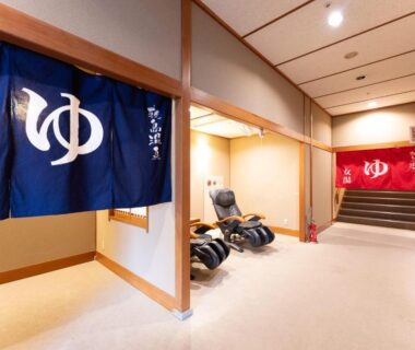Corridor with blue and red onsen noren, massage chairs and wooden interior at Healthy Pal Akagi in Gunma
