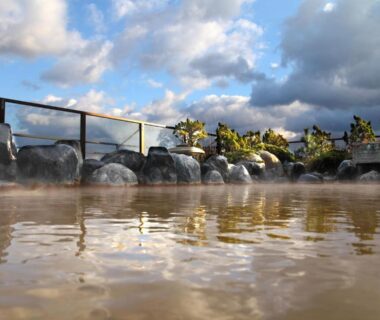 Steaming outdoor onsen bath with rock edging and cloudy sky at Heiseikan Kaiyotei, Hokkaidō Japan